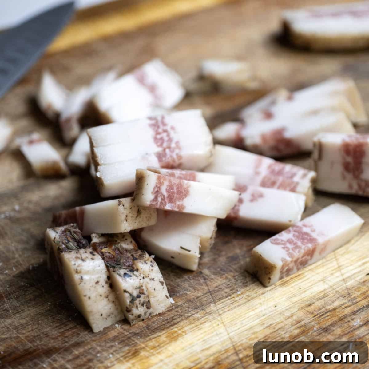 Pasta Alla Gricia: Rome's Simple Perfection 4 Perfectly diced guanciale, ready for rendering, on a wooden cutting board.