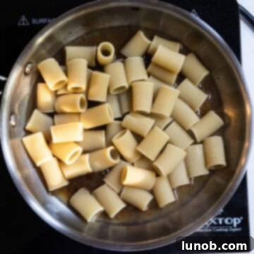 Pasta Alla Gricia: Rome's Simple Perfection 8 Half-cooked rigatoni pasta being added to the pan with the guanciale fat and pasta water.