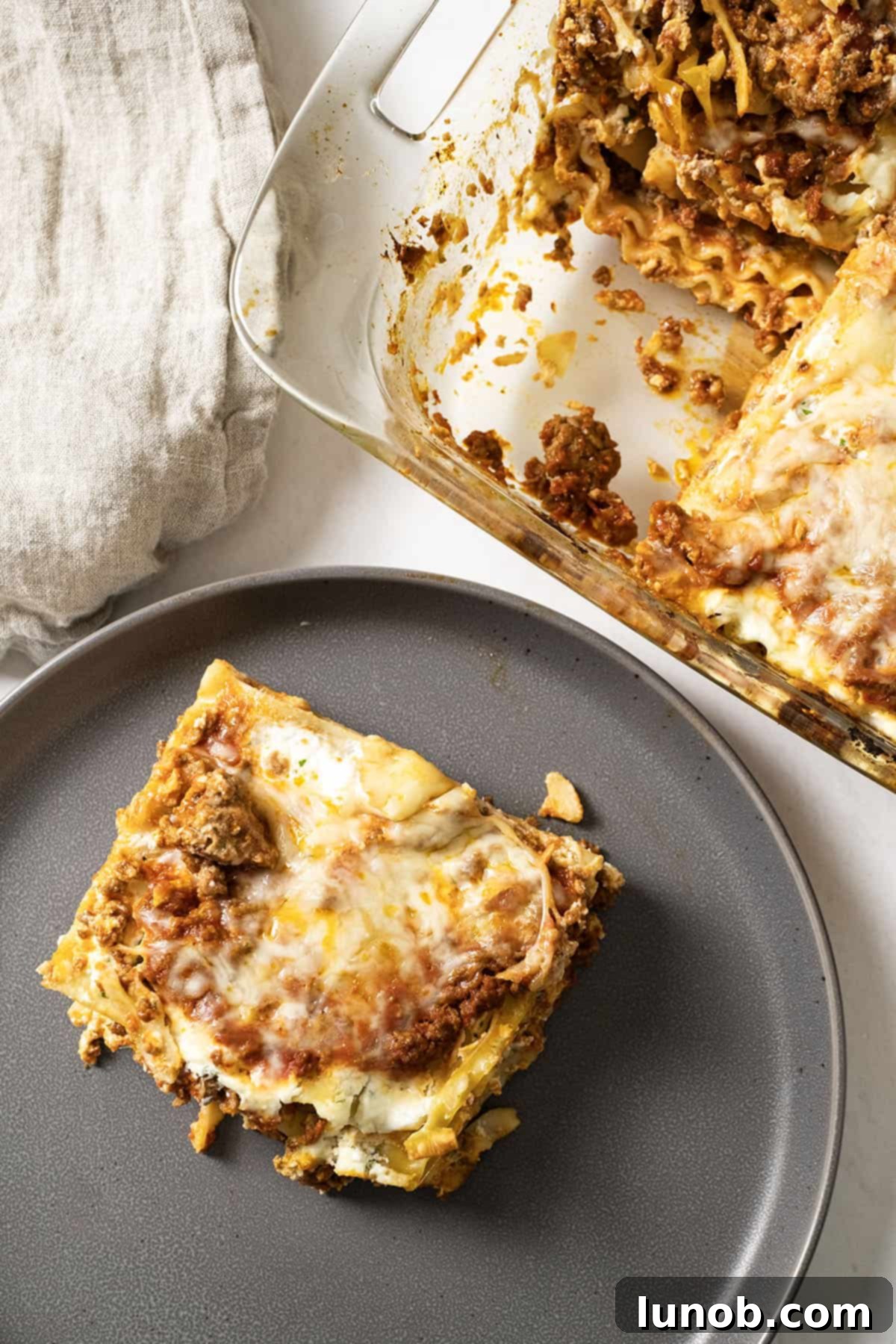 A beautifully presented square of authentic Italian lasagna on a plate, with the full baking dish blurred in the background.