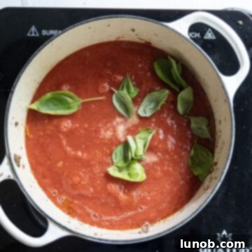 Tomato puree simmering in the pot, topped with fresh basil leaves.