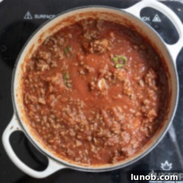 The browned meat being added back into the simmering tomato sauce in the Dutch oven.