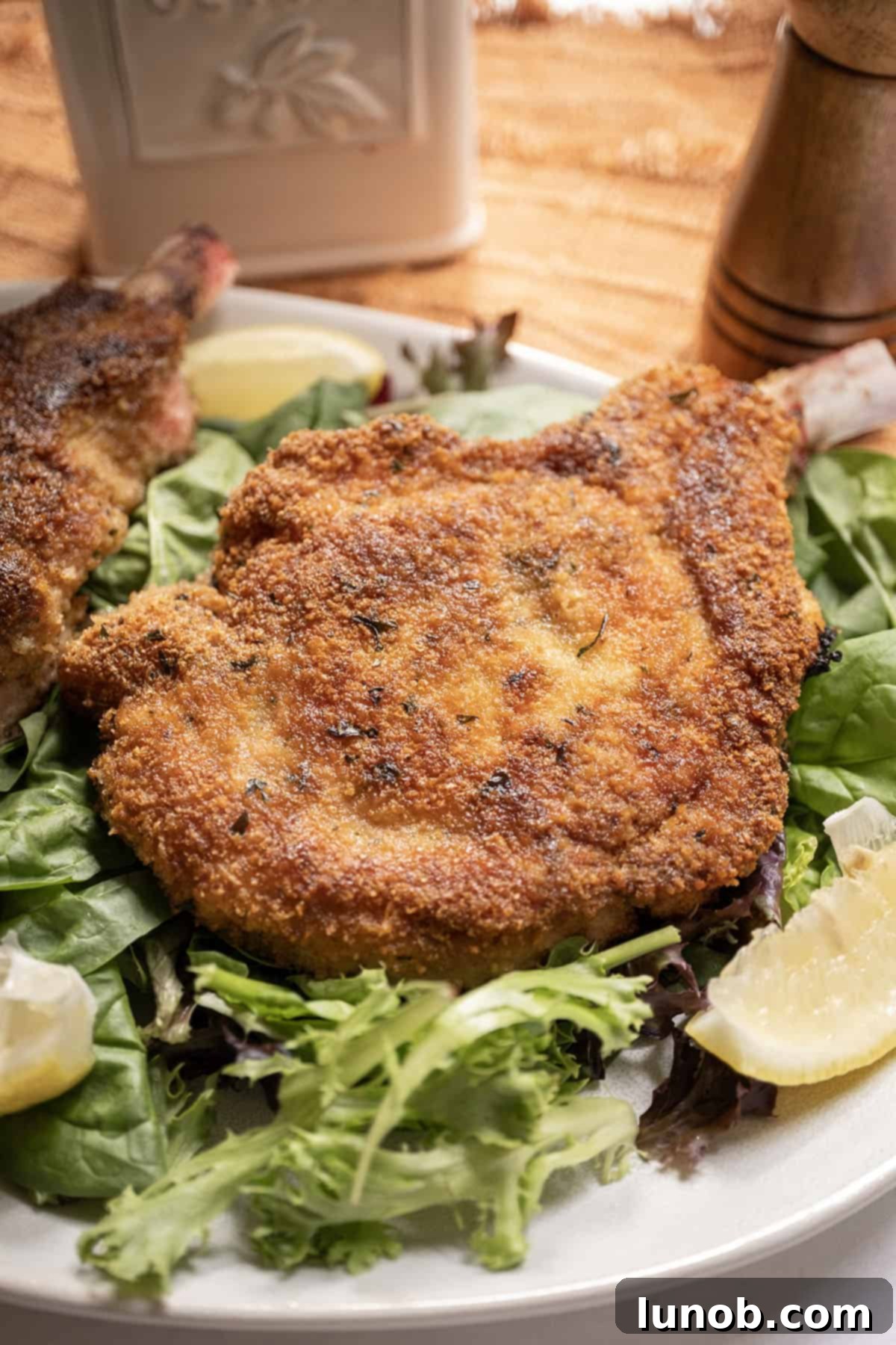 Golden Crispy Milanese Pork Chop 2 Pork chop milanese over a greens salad and a wedge of lemon on the side.