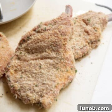 Golden Crispy Milanese Pork Chop 6 Pork chops dredged in bread crumbs on a cutting board.