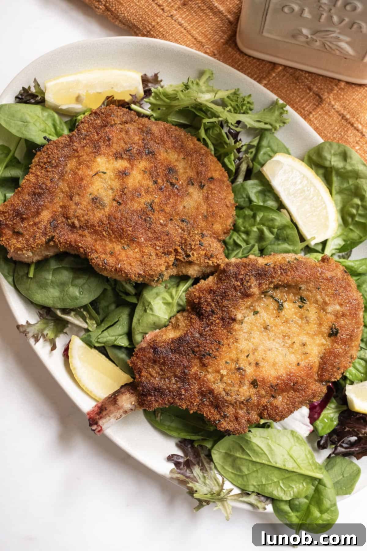 Golden Crispy Milanese Pork Chop 9 Pork chop milanese over a greens salad and a wedge of lemon on the side.
