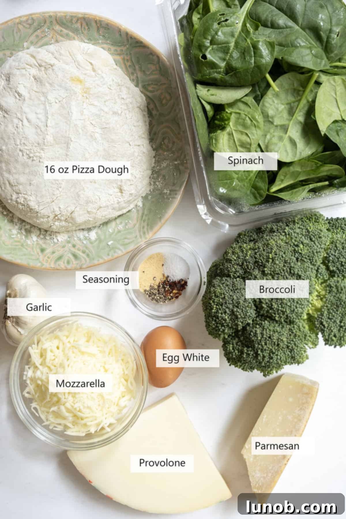 Fresh ingredients for veggie pinwheels, including pizza dough, broccoli, spinach, and Italian cheeses.