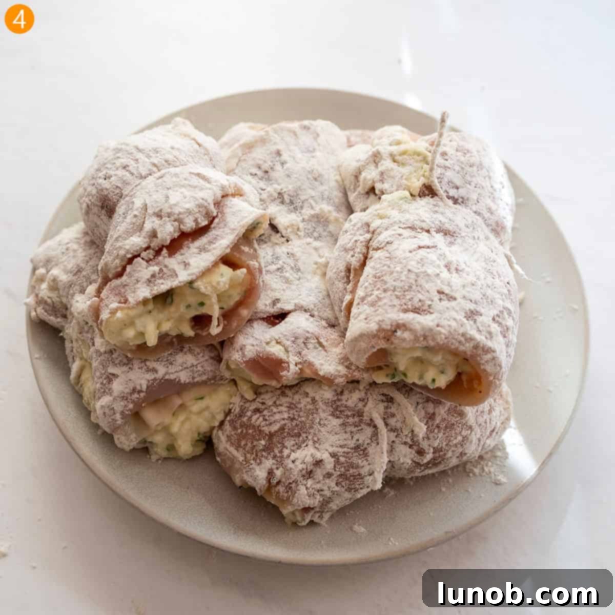 Chicken rollatini pieces being dredged thoroughly in flour for an even coating.