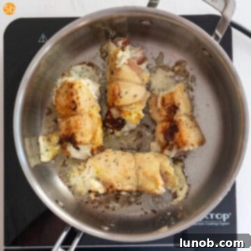 A chicken rollatini piece flipped, showing a golden brown seared side in the pan.