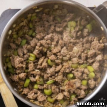 Ultimate Italian Sausage Stuffed Mushrooms 6 Italian sausage browning in a pan with cooked vegetables, being broken up with a wooden spoon.