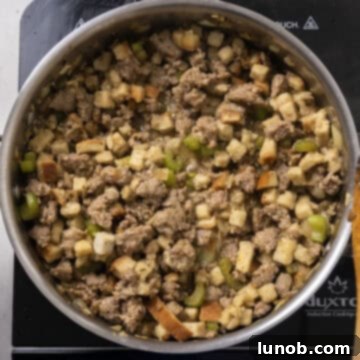 Ultimate Italian Sausage Stuffed Mushrooms 7 Cube stuffing and chicken broth being combined with browned sausage and vegetables in a pan.