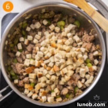 Savory Italian Sausage Thanksgiving Stuffing 7 Dry bread stuffing cubes being added to the browned sausage and vegetable mixture in a large saucepan.