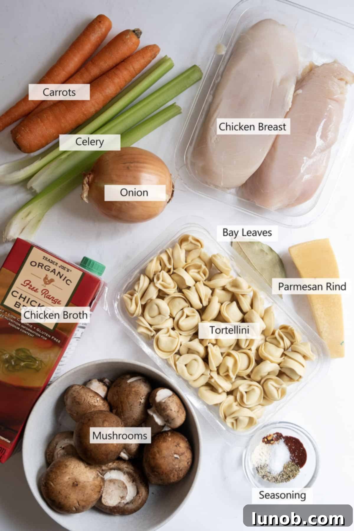 Comforting Chicken Tortellini Soup 3 A collection of fresh ingredients laid out, including chicken breast, chopped vegetables, mushrooms, broth, and various seasonings, for making chicken tortellini soup.