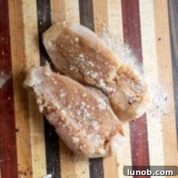 Comforting Chicken Tortellini Soup 4 Chicken breast being seasoned on a cutting board with a mix of spices.