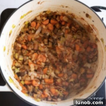 Soul-Warming Sausage and Lentil Soup 6 Vegetables including mushrooms, carrots, and red pepper sautéing with tomato paste, which is caramelizing at the bottom of the pot.