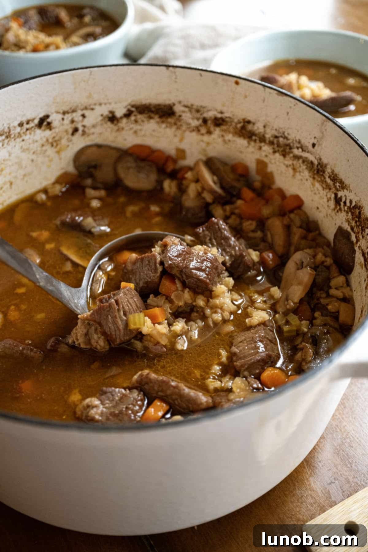 A large pot filled with rich, simmering beef and barley soup, showcasing chunks of beef, vegetables, and barley. 