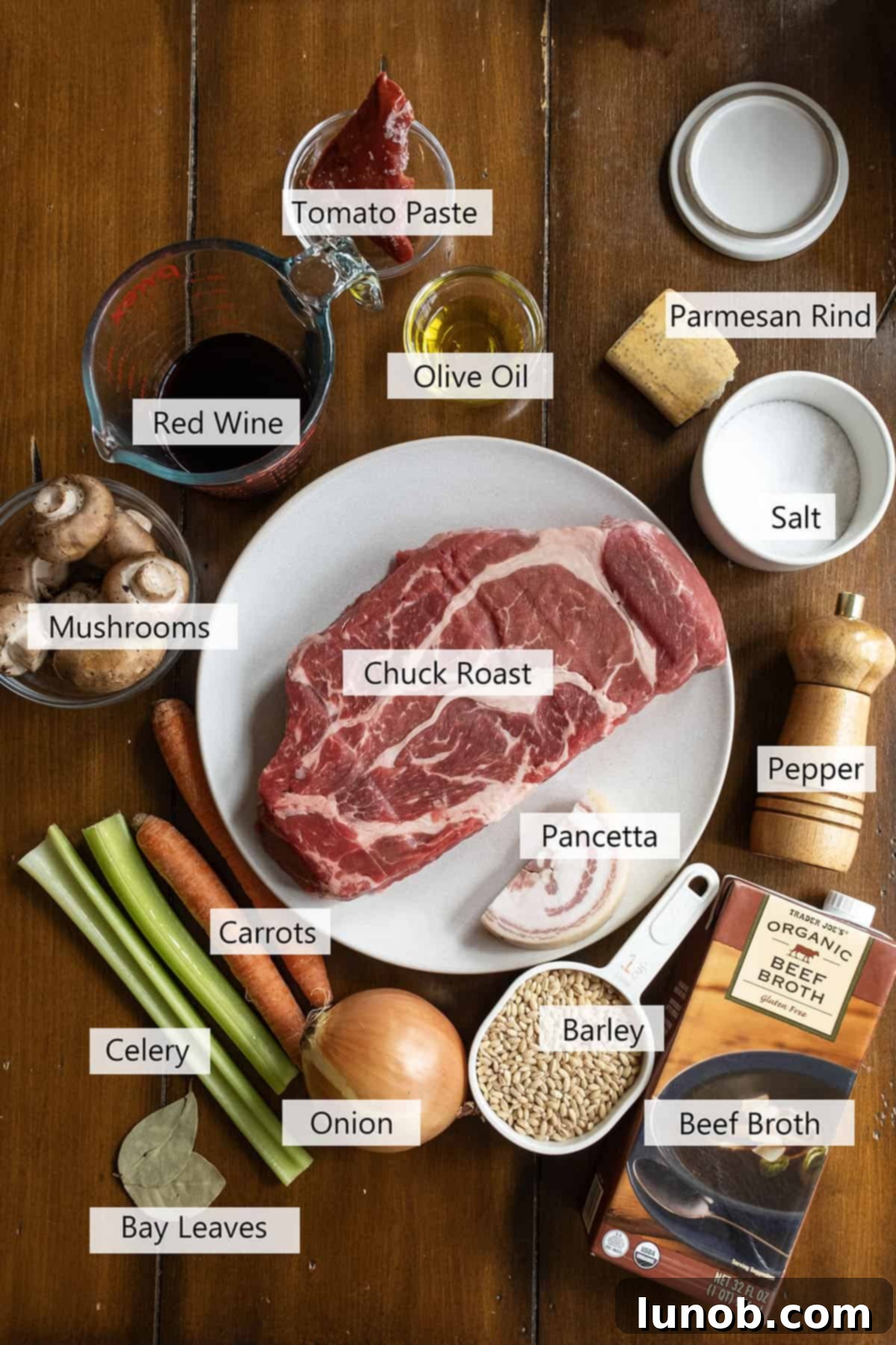 A rustic spread of fresh ingredients for beef and barley soup, including chuck roast, colorful vegetables, barley, and spices.