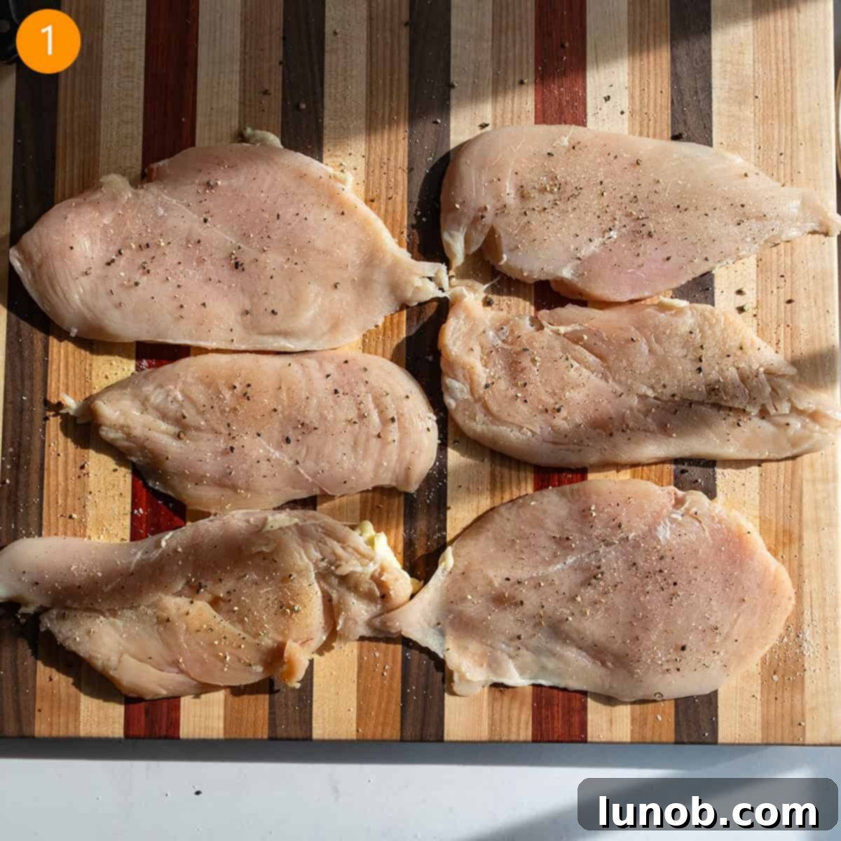 Tenderized chicken breast seasoned with salt and pepper on a cutting board. 