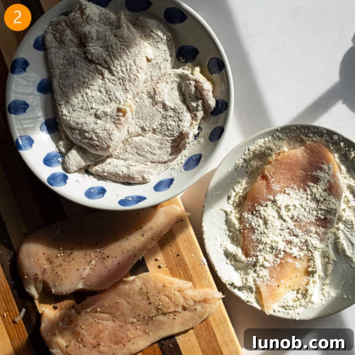 Dredging chicken breast in flour on a plate.