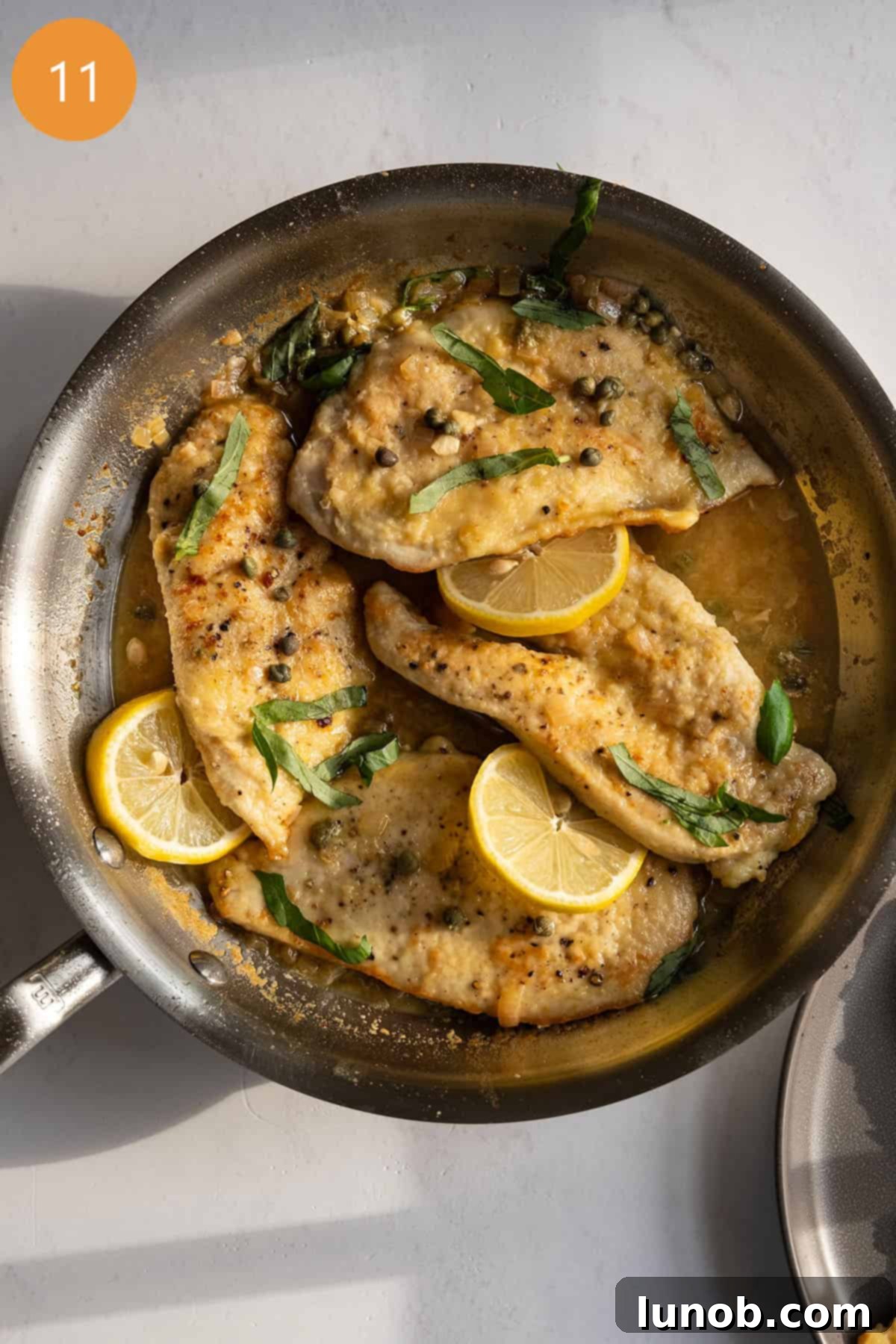 Chicken piccata in sauce pan topped with basil and capers.