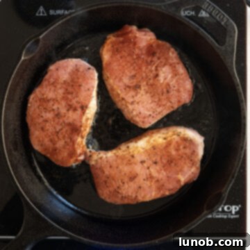 Ultimate Cast Iron Boneless Pork Chops 6 A boneless pork chop searing in a hot cast iron skillet, developing a golden crust.