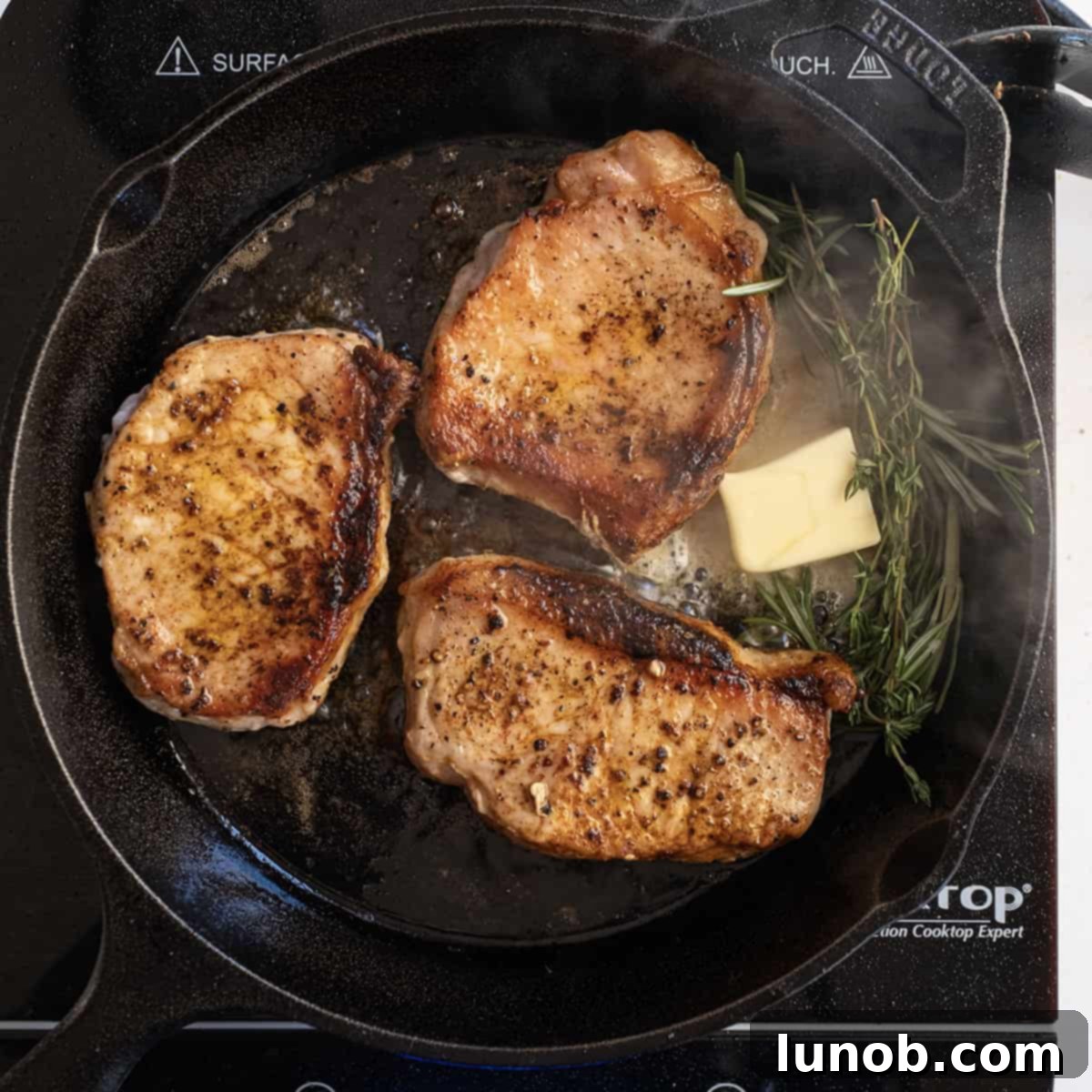 Ultimate Cast Iron Boneless Pork Chops 8 Cooked boneless pork chops being basted with melted butter, fresh thyme, and rosemary in a cast iron skillet.