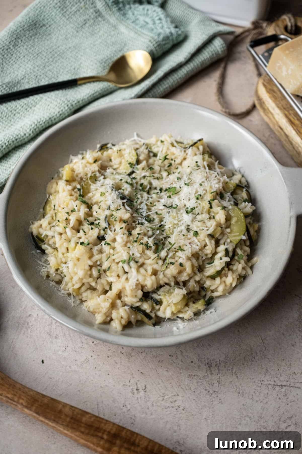 Zucchini risotto in a bowl topped with parmigiano and parsley.