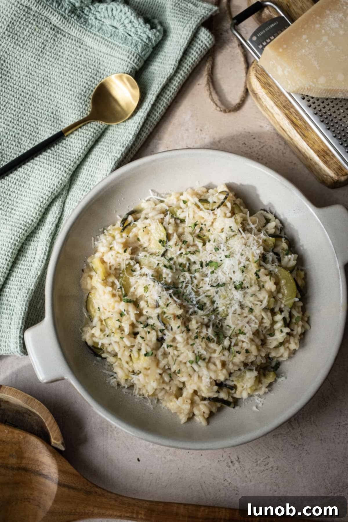 Zucchini risotto in a bowl topped with parmigiano and parsley.