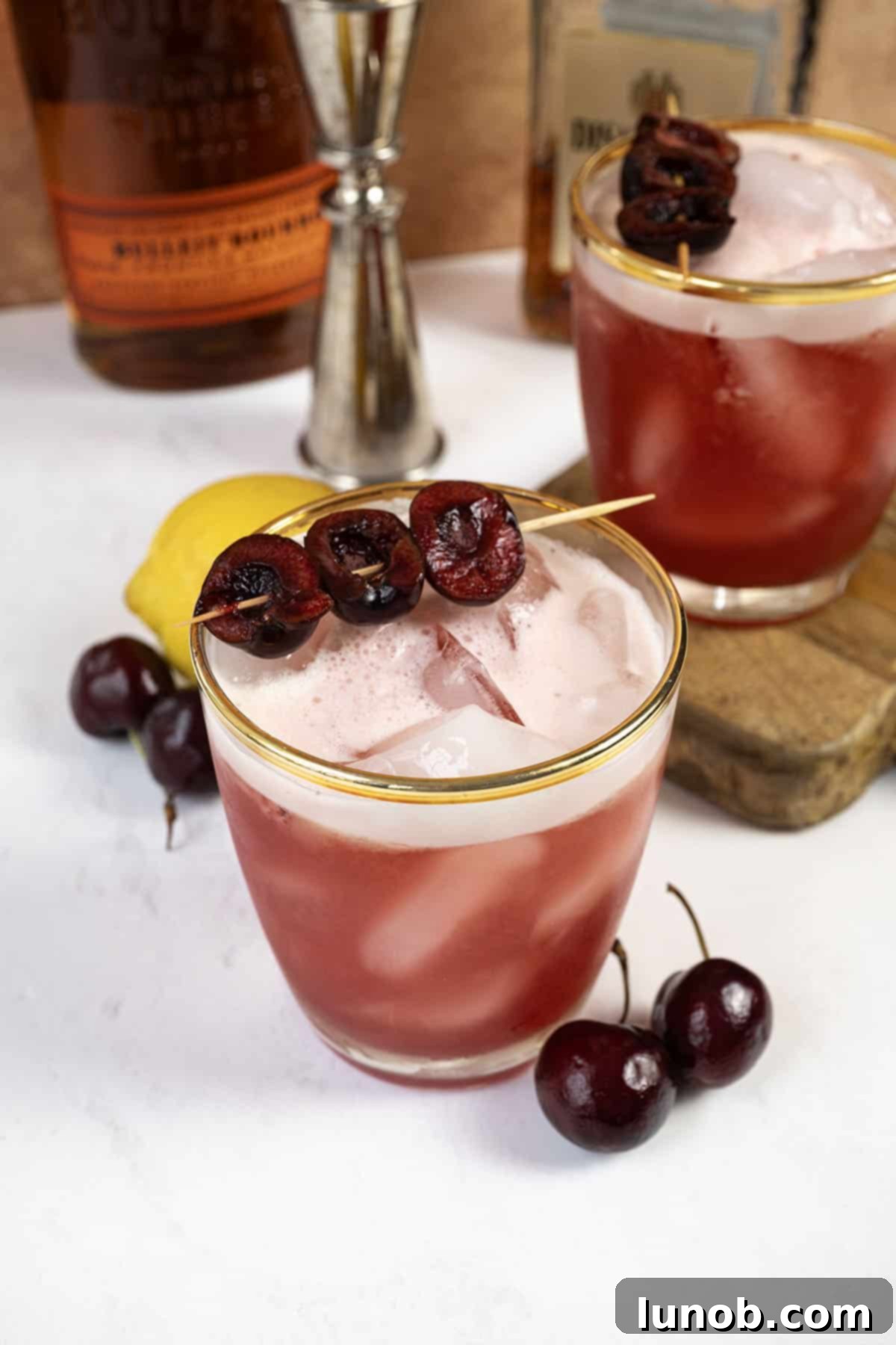 A vibrant red Cherry Amaretto Sour cocktail in a coupe glass, garnished with fresh cherries on a pick.