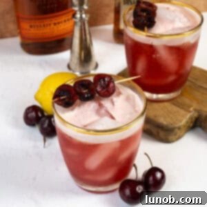 A Cherry Amaretto Sour cocktail in a glass with a cherry garnish, displaying its vibrant red color and frothy top.
