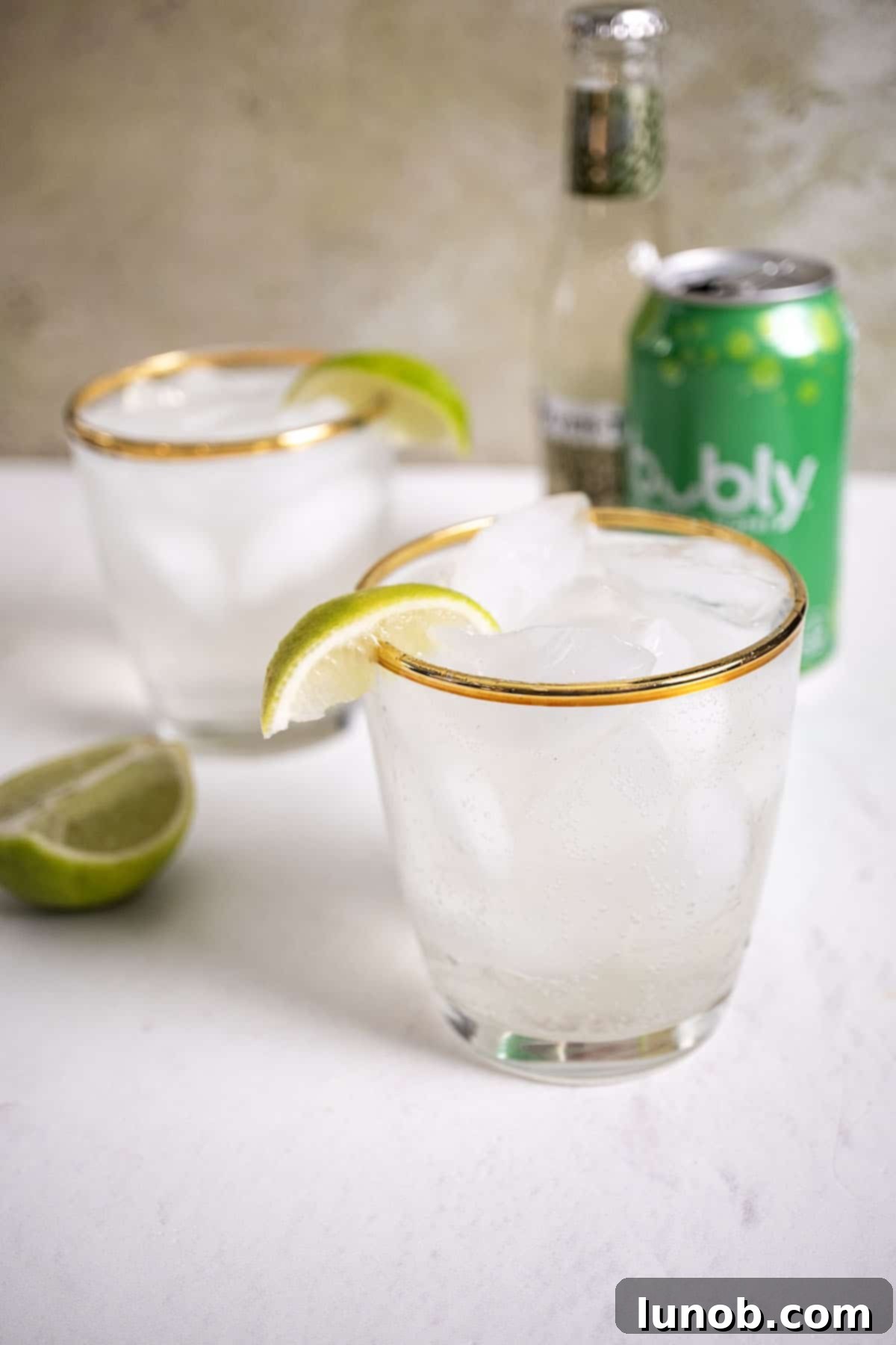 Two glasses of non-alcoholic Moscow Mules, garnished with lime wedges, alongside a fresh lime and a can of seltzer.