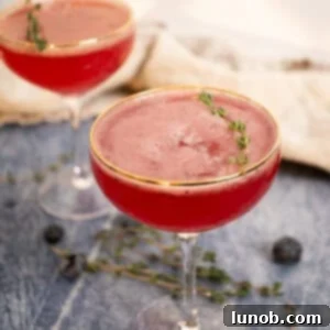 Blueberry Blitz Mocktail 5 Two vibrant blueberry mocktails, each garnished with a sprig of thyme, are presented in elegant glasses.