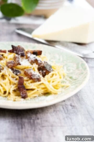 The Art of Perfect Carbonara 13 Finished spaghetti carbonara on a plate topped with extra pecorino and black pepper, made with guanciale.