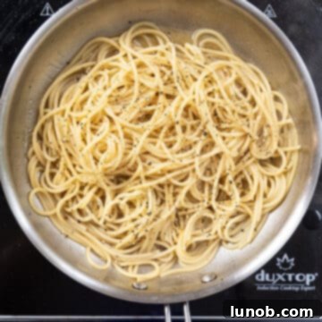 The Art of Perfect Carbonara 8 Hot spaghetti added to the saucepan with black pepper, being tossed to coat.