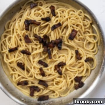 The Art of Perfect Carbonara 10 Crispy guanciale being returned to the pan with the creamy spaghetti carbonara, ready for final toss.