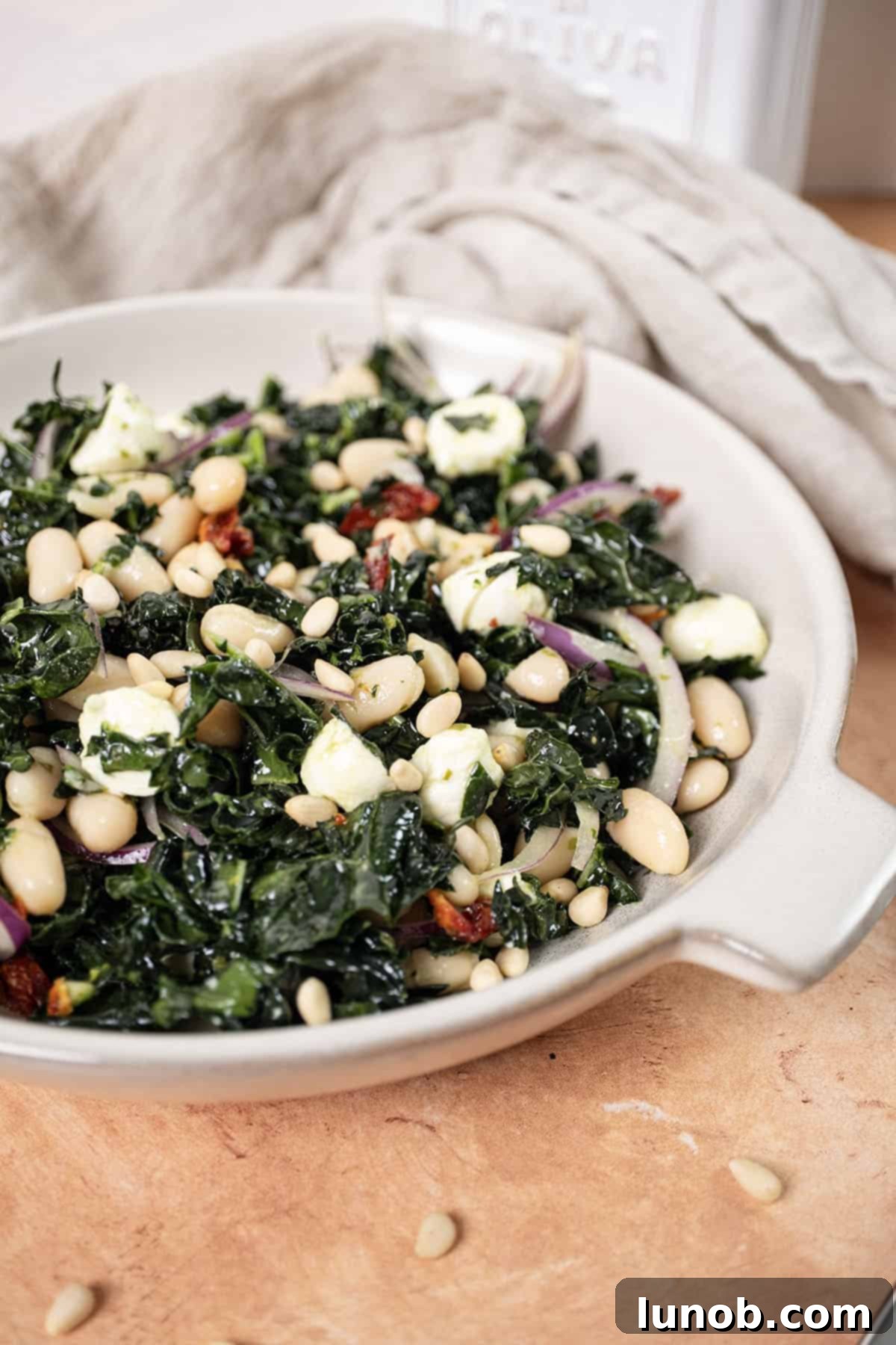 A vibrant bowl of Kale and Cannellini Bean salad, garnished with a sprinkle of pine nuts and fresh basil.