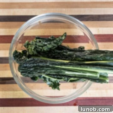Hands gently massaging fresh lacinato kale with a drizzle of olive oil in a large mixing bowl.