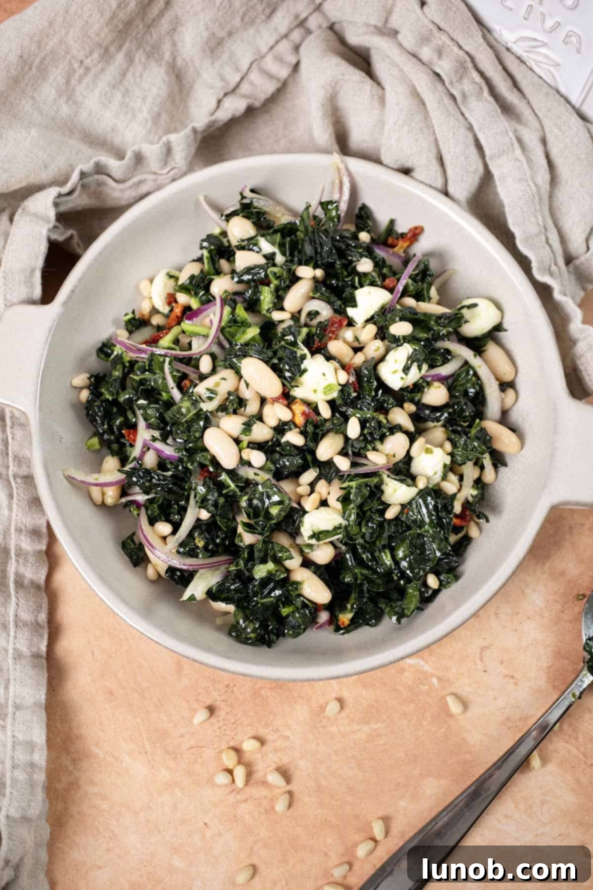 A beautifully presented, chilled Kale and Cannellini Bean salad in a large serving bowl, elegantly topped with toasted pine nuts.