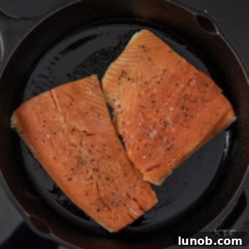 Salmon fillet being placed skin-side down in a hot cast iron skillet with shimmering avocado oil.