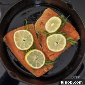 Dill and lemon slices placed on top of salmon searing skin-side down in a cast iron pan.