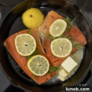 Salmon being basted with melted butter and garlic in a cast iron skillet.