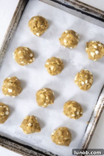 Soft Baked White Chocolate Macadamia Delights 9 Cookie dough rolled into uniform balls and arranged on a parchment paper-lined baking sheet, ready for chilling.