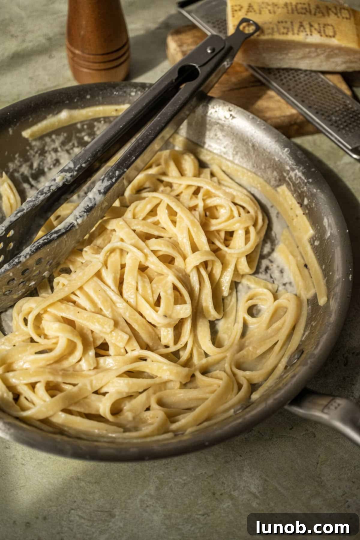 Traditional Roman Fettuccine Alfredo 2 Fettuccine in alfredo sauce in a pan with tongs, ready to be served.
