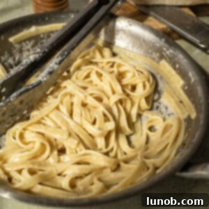 Fettucine in alfredo sauce in a pan with tongs, garnished with fresh pepper.