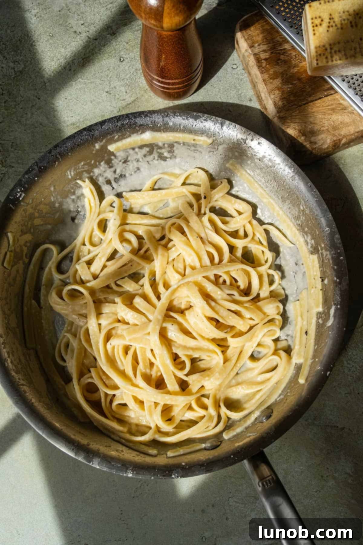 Traditional Roman Fettuccine Alfredo 10 Fettuccine alfredo in a pan, garnished with fresh parsley, with extra Parmigiano and pepper on the side.