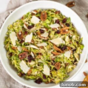 Brussels sprouts salad in a bowl topped with dried cranberries and pecans.
