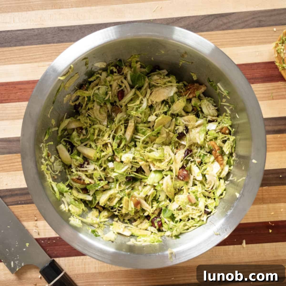 Crispy Pancetta Brussels Sprout Salad 9 The chopped Brussels sprouts salad being tossed with the balsamic vinaigrette dressing in a large bowl.
