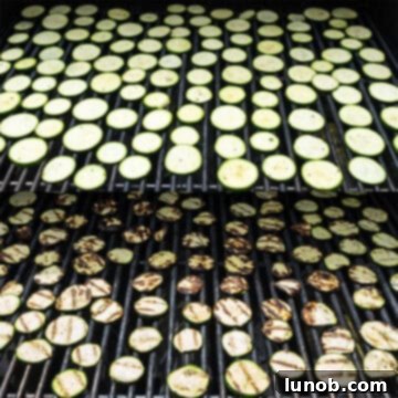 Minty Marinated Zucchini 7 Zucchini slices grilling on a hot barbecue, showing char marks and bubbling texture.