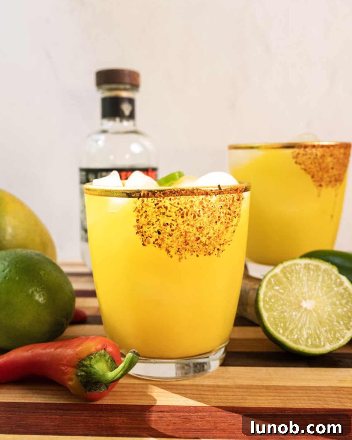 Sizzling Mango Margarita 2 A vibrant spicy mango margarita garnished with a lime wheel and surrounded by fresh jalapenos and limes.