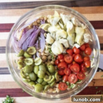 Vibrant Orzo and Chickpea Salad 8 Adding red onion, olives, artichokes, and grape tomatoes to the bowl with orzo and beans.
