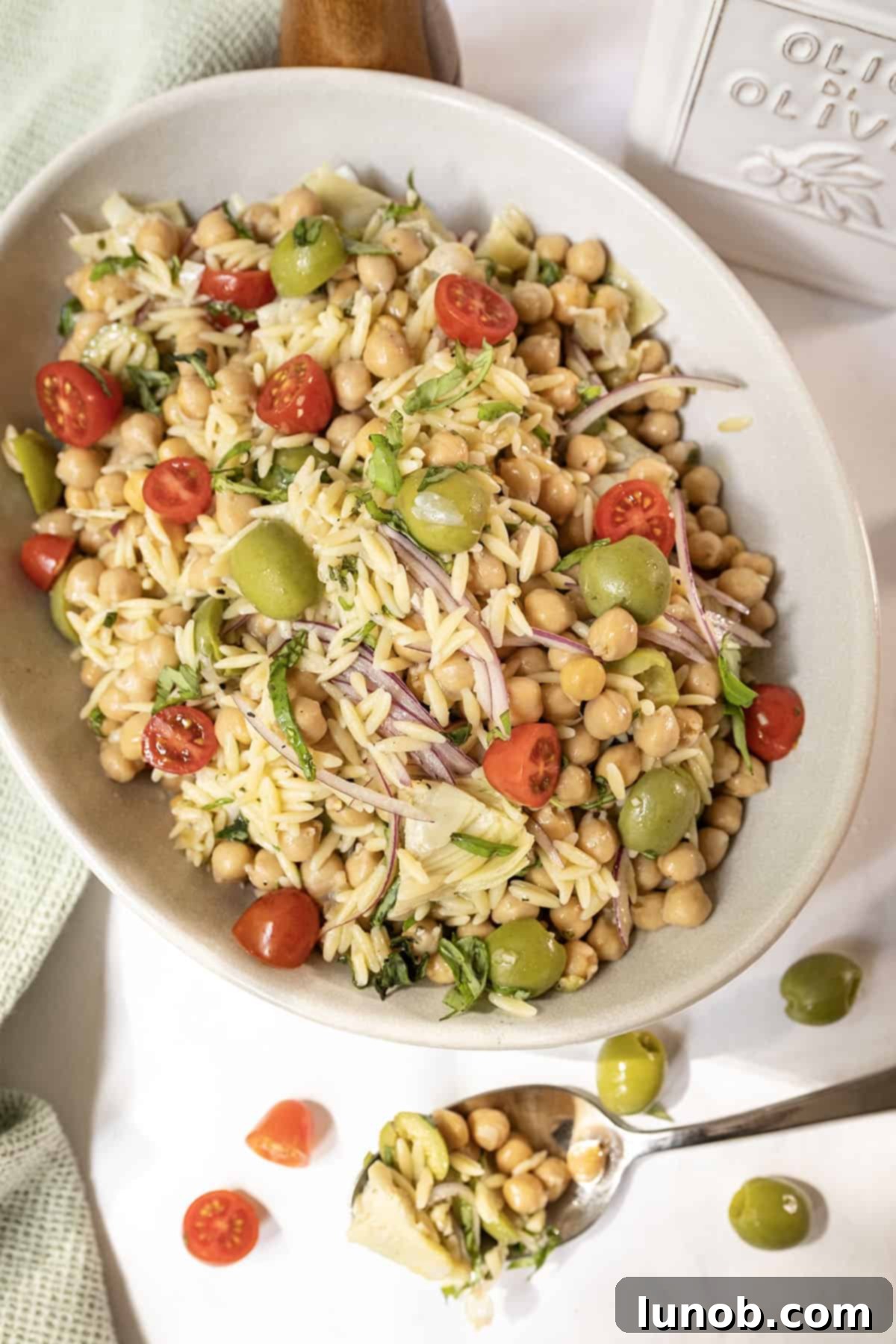 Vibrant Orzo and Chickpea Salad 10 A large bowl of Orzo and Garbanzo Bean Salad, garnished with fresh basil and ready to be enjoyed.