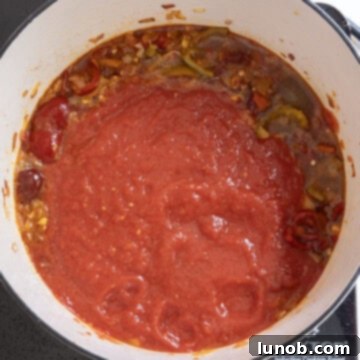 Fiery Chicken Rigatoni 10 Crushed tomatoes being stirred into the reduced spicy base in the saucepan, creating a rich red sauce.